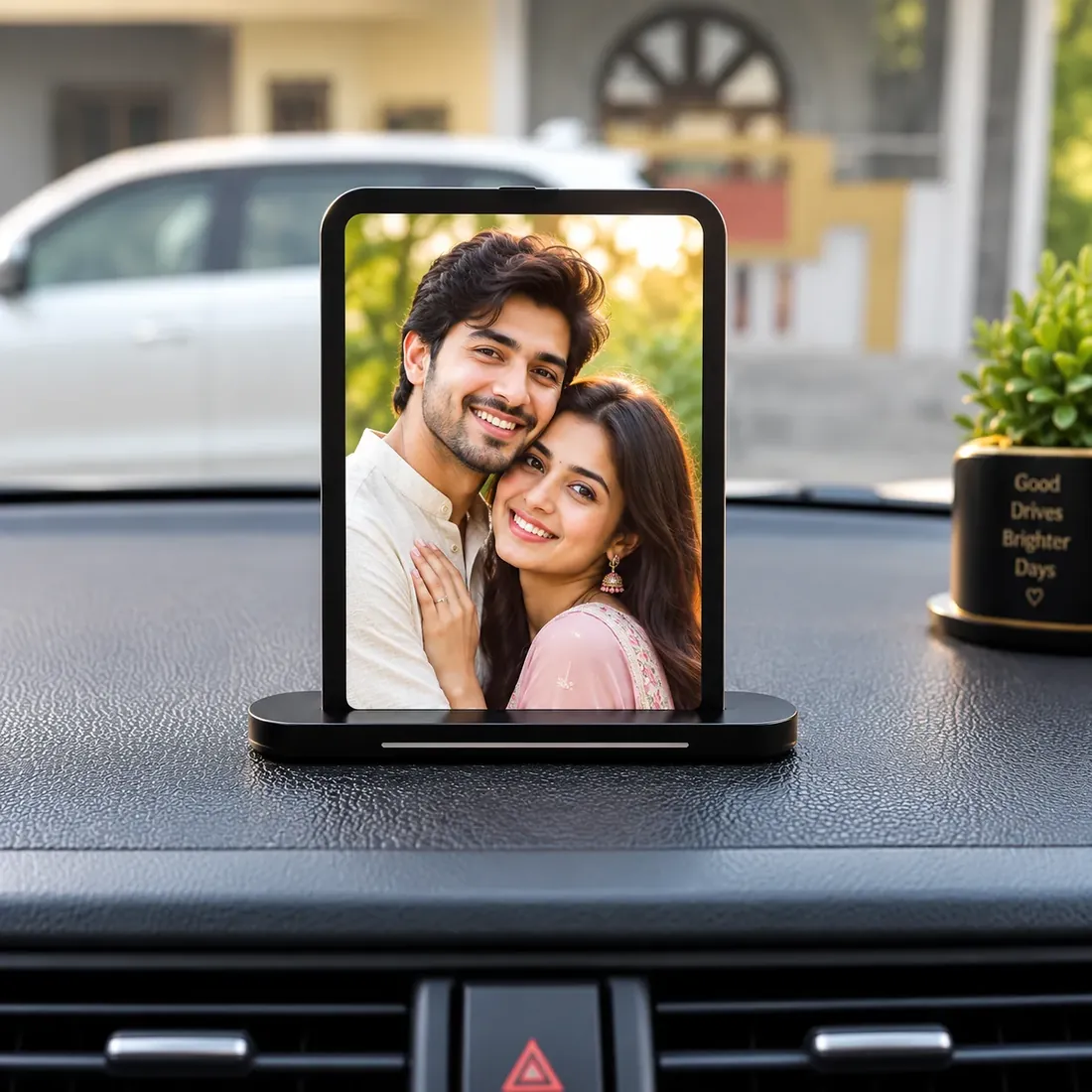 Black acrylic photo stand on a car dashboard, printed with a couple’s portrait on a weighted non-slip base — Siri Print World, Palakollu