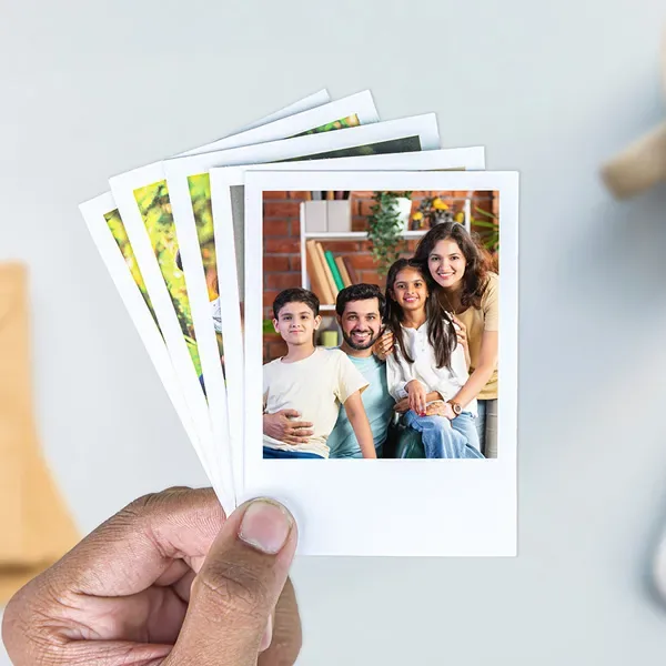 A hand holding a fanned stack of glossy photo prints, the front one showing a family at home — Siri Print World, Palakollu